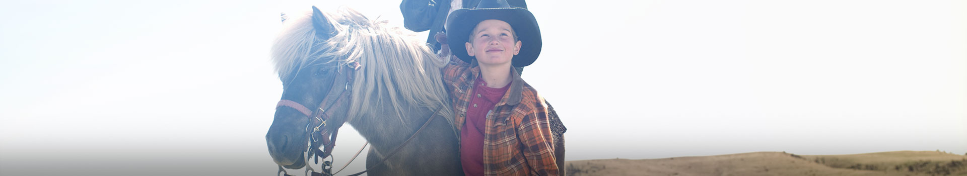 young boy in cowboy hat standing by pony